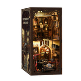 Miniature workshop diorama kit with open dark case, showing shelves, tools, and machinery