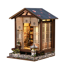 Wooden mini book nook house with peaked roof, open panels, and warm-lit interior
