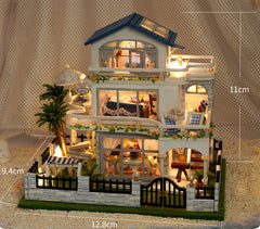 Miniature two-story dollhouse model with blue roof, illuminated windows, and garden fence