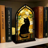 Stained-glass style black cat book nook with arched window and warm candle glow