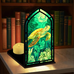Book nook display with illuminated sea turtle panel, black base, and glowing candle beside it