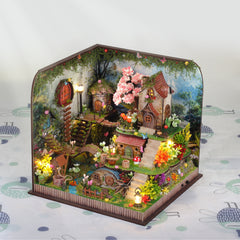 Miniature forest cabin diorama with pink blossoms, lantern lights, and tiny garden