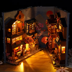 Japanese-style book nook diorama with lit buildings, lanterns, and pink cherry blossoms