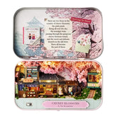Tiny spring cherry blossom diorama in a small metal tin, opened to village scene