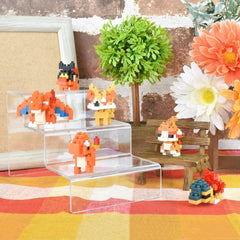 A collection of pixel art figurines, including a dragon, cat, and other small characters, arranged on a wooden bench and a colorful plaid tablecloth.