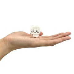 A hand holding a small white toy figure with a face and eyes.