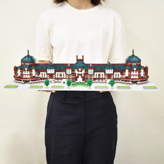 A person is holding a large, intricate model of a building made out of small, colorful bricks.