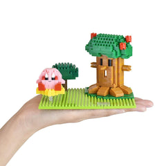 A hand holding a green and yellow Lego tree and a pink Lego character on a green Lego baseplate.