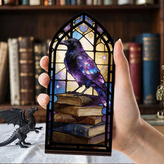 Hand holding arched book nook candle display with purple raven on book stack