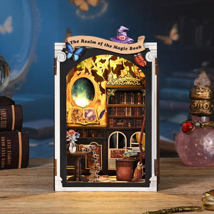 A miniature diorama depicting a fantasy-themed room with a bookshelf, a table with a vase of flowers, and a wizard's hat on a shelf. The room appears to be part of a larger fantasy world, as indicated by the "The Realm of the Magic Book" banner above the diorama.