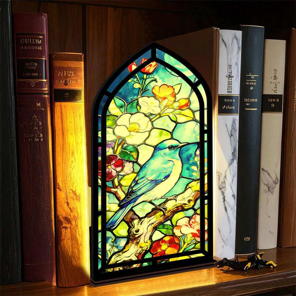 Arched bluebird stained-glass book nook with black frame, standing between books
