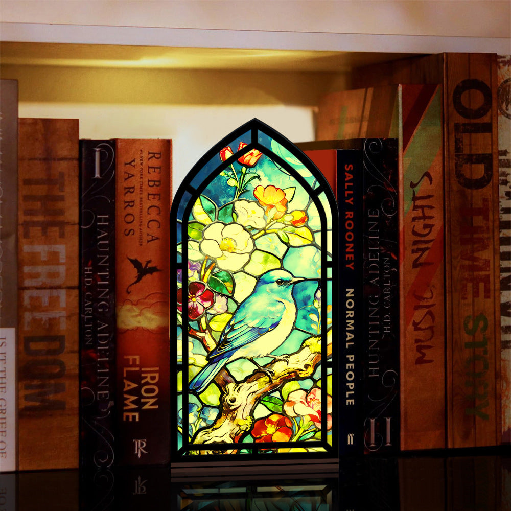 Stained-glass style book nook display with bluebird, flowers, and branches in black frame