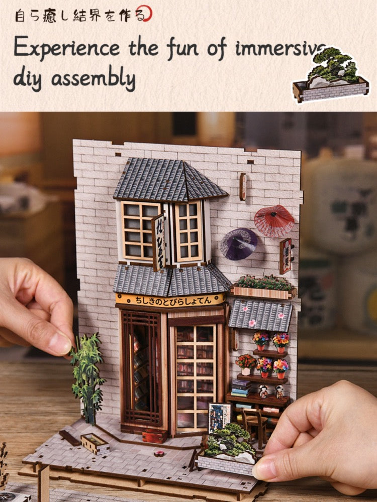 The image is a collage of two photos. The top photo shows a miniature wooden bookshelf with a small house and other details, while the bottom photo depicts a person assembling a small wooden model of a house.