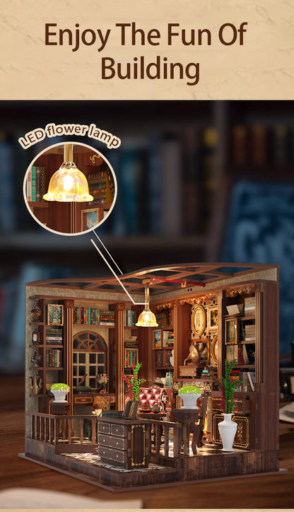 The image is a miniature model of a building with a library-like atmosphere, featuring bookshelves, a desk, and a lamp.