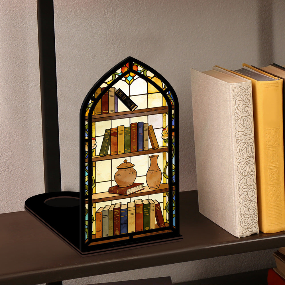 Arched illuminated book nook on a shelf surface with faux books, teapot, and vase.