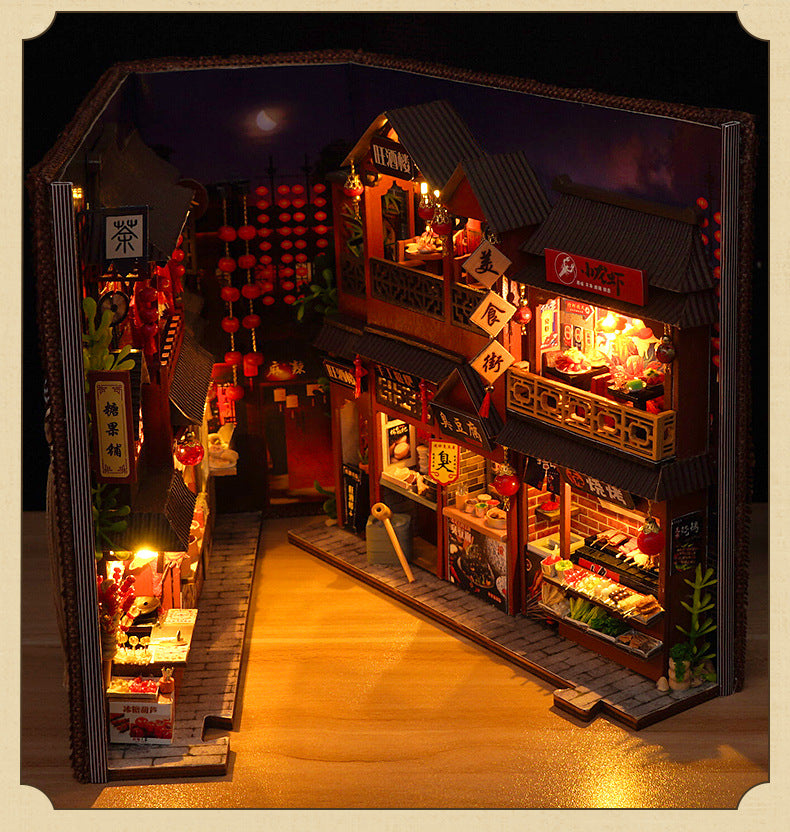 Miniature book nook kit open with central walkway, glowing storefronts, and hanging red lanterns