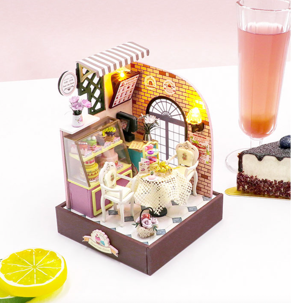 Light-up miniature cake station diorama with brick arch, striped awning, small table and chairs