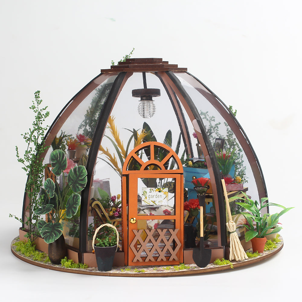 Miniature greenhouse house kit on a round base with arched frame, orange door and plants
