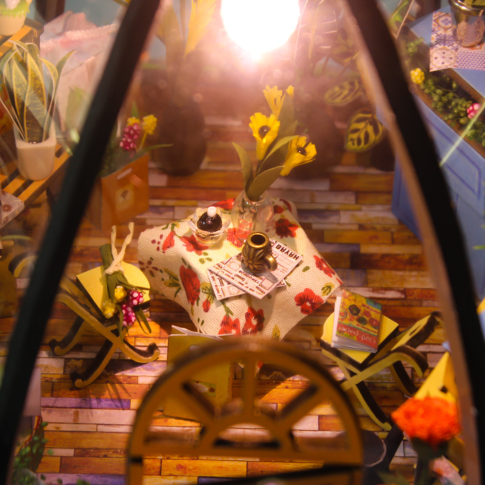 Miniature greenhouse interior with wooden steps, decorated table, and warm lamp glow.
