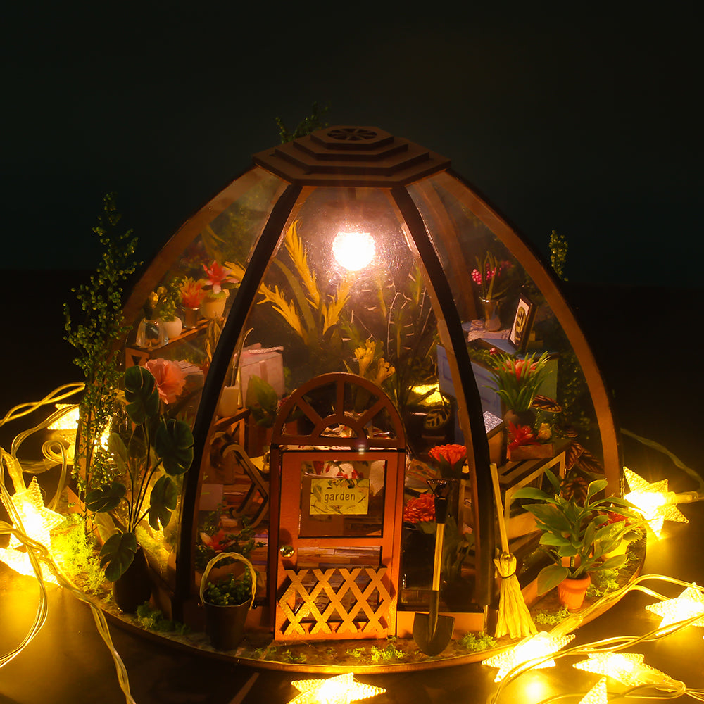 Miniature greenhouse house kit with warm string lights glowing around potted plants