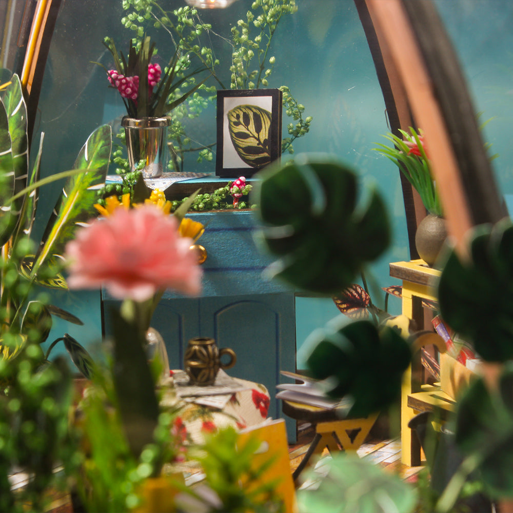 Mini greenhouse interior closeup of potted plants, table decor, and window view.