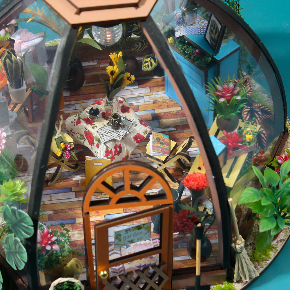 Miniature greenhouse house kit with dark frame and orange wheel-door, packed with tiny plants