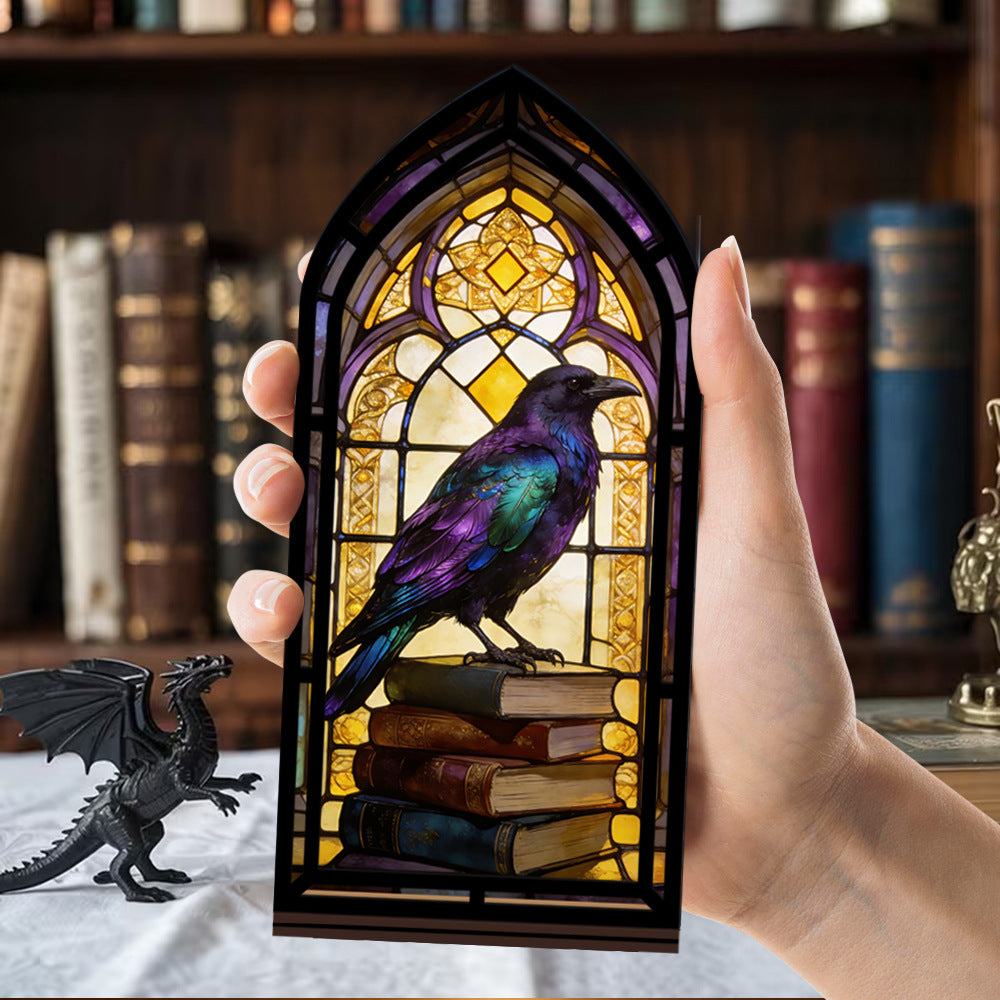 Hand holding an arched book nook with glowing stained-glass raven perched on books