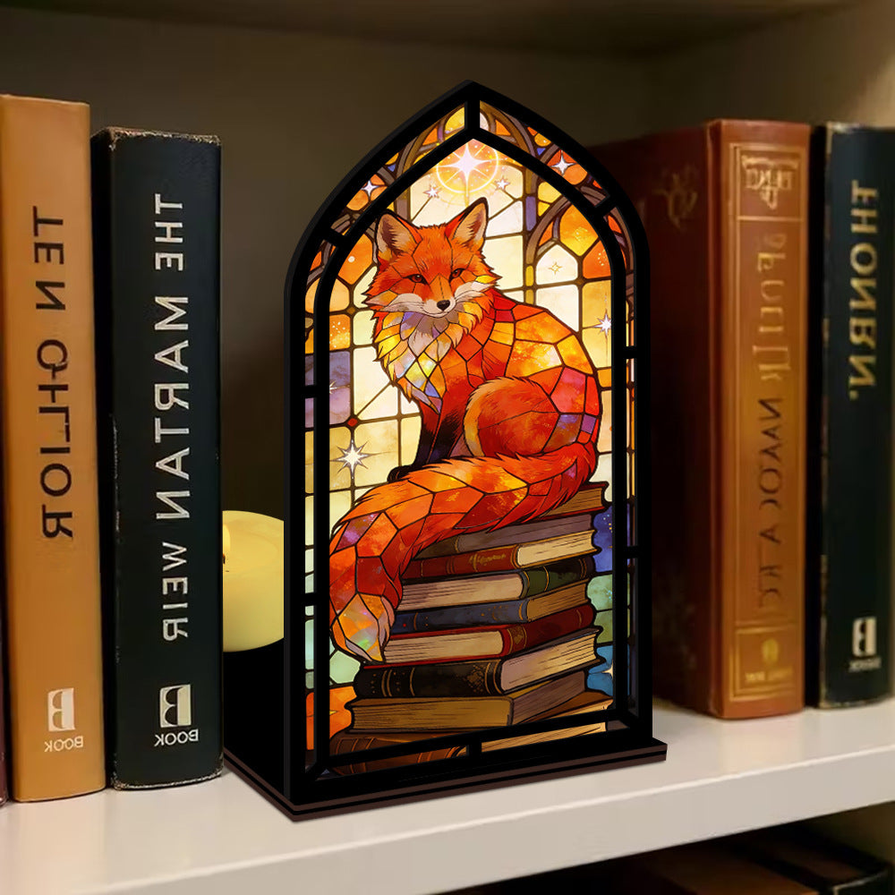 Stained-glass fox book nook in black arched frame with stacked books and warm glow