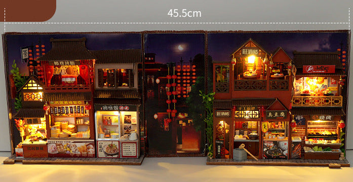 Miniature book nook kit open with extended view of illuminated night market shelves and counters