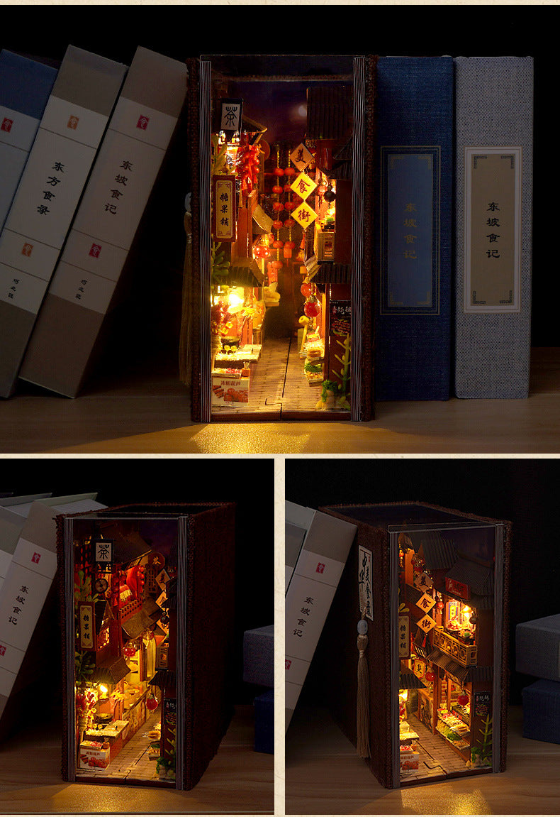 Miniature book nook kit with door panels open, showing illuminated night market shops and food displays