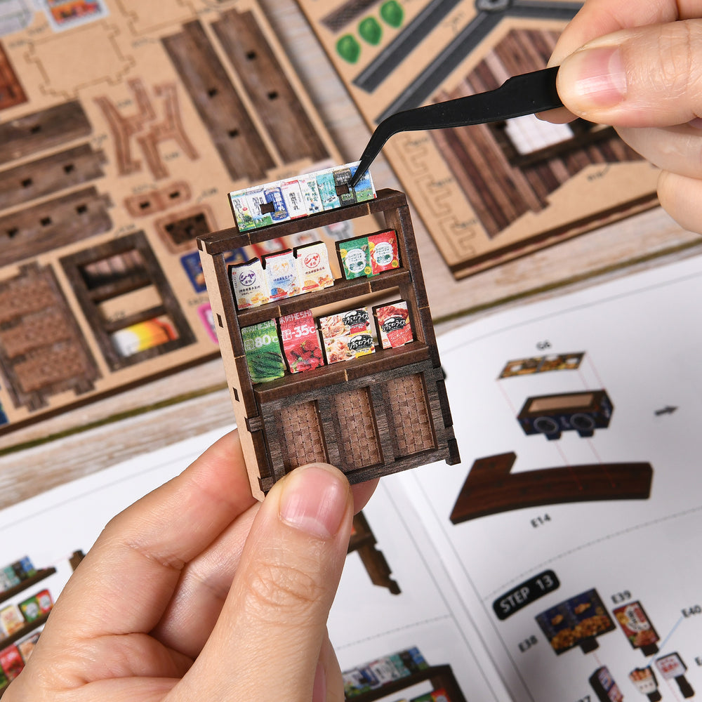Miniature storefront cabinet being assembled, held in hands with product shelves