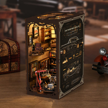 A miniature model of a workshop, featuring various tools and equipment, including a car and other objects, displayed in a wooden box with a decorative border.