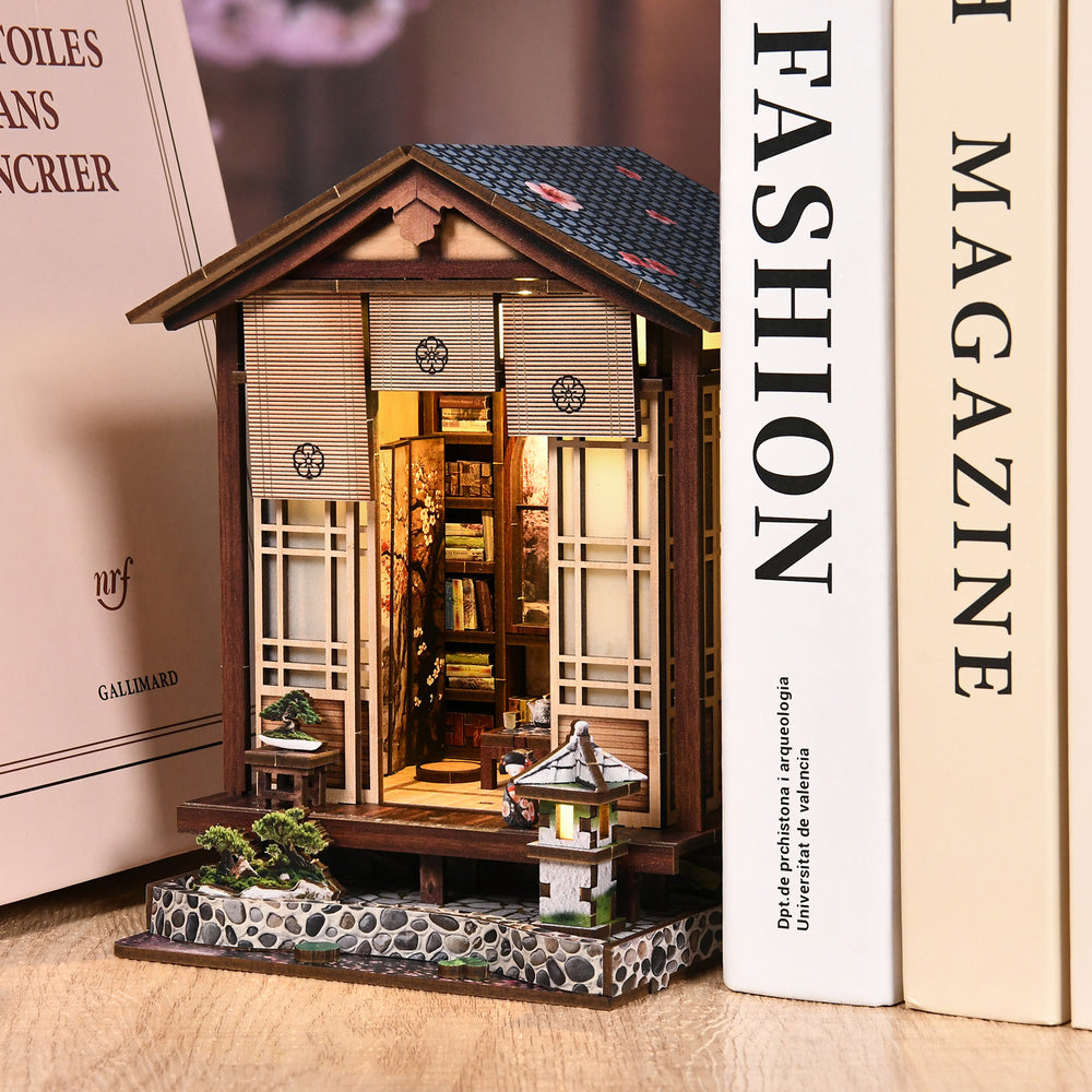 Wooden mini book nook house next to product boxes, with lit interior and lantern porch