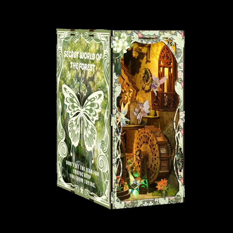 The image is a miniature diorama or model of a forest, featuring various elements such as a butterfly, a wheel, and flowers. The diorama is set within a decorative frame, giving it a whimsical and enchanting appearance.