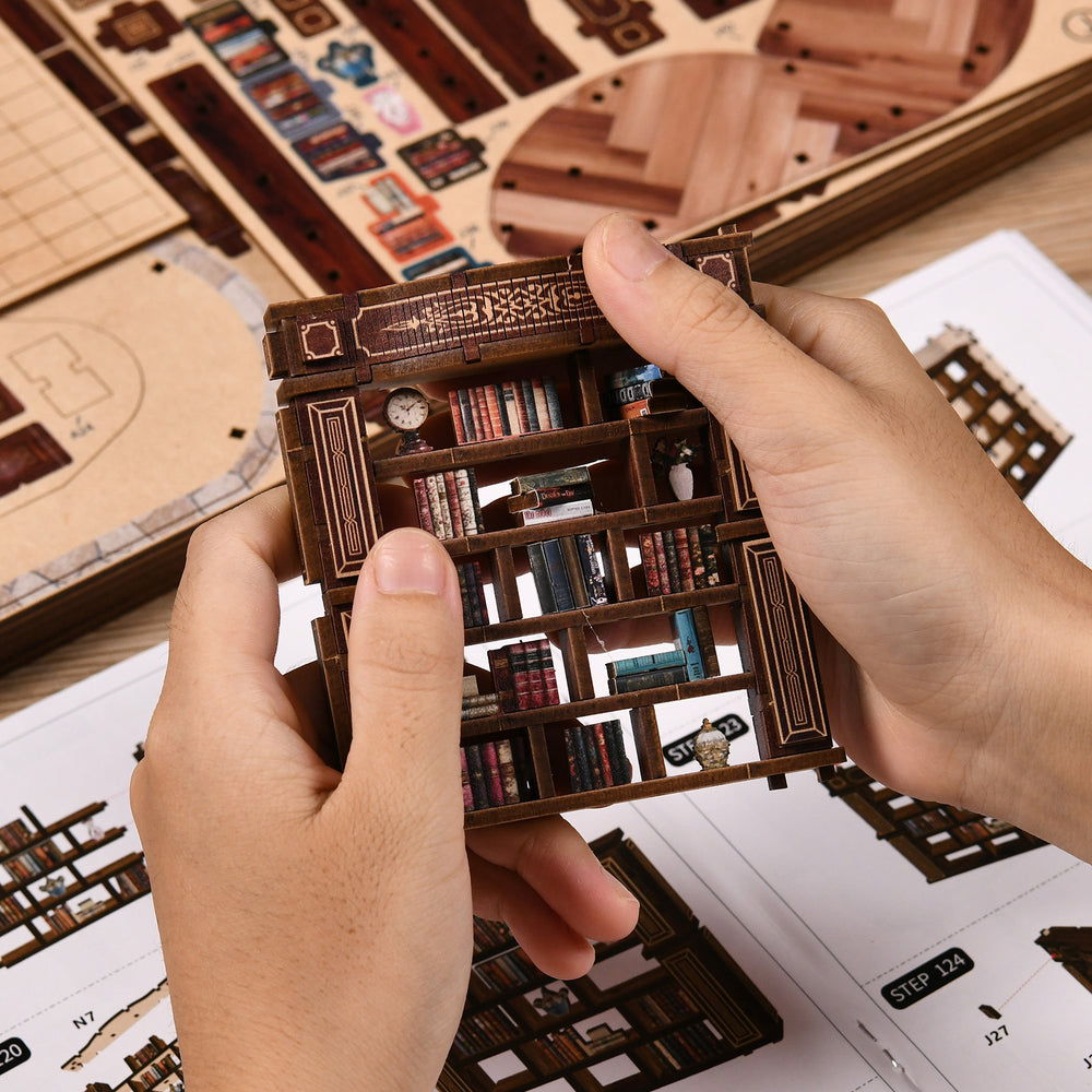 Hands assembling wooden mini house library module with book shelves and small parts