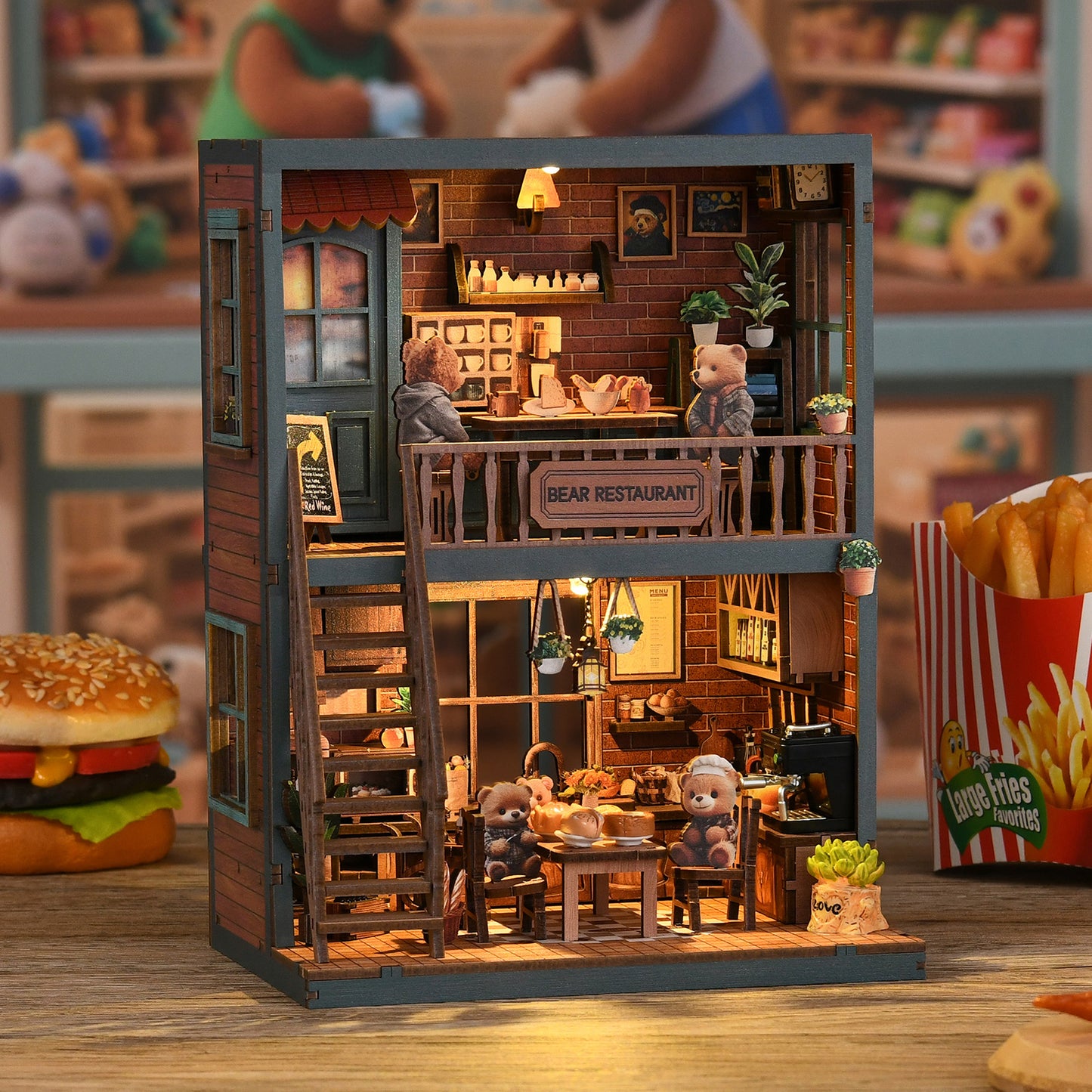 A miniature model of a bear-themed restaurant, complete with a dining area, kitchen, and seating for several teddy bears. The restaurant is decorated with various elements such as potted plants, a sign, and a menu board. The scene is set on a table, and there are also some food items, including a hamburger and a container of fries, placed nearby.