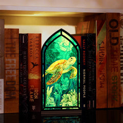 Book nook display with stained-glass style sea turtle scene in a black arched frame