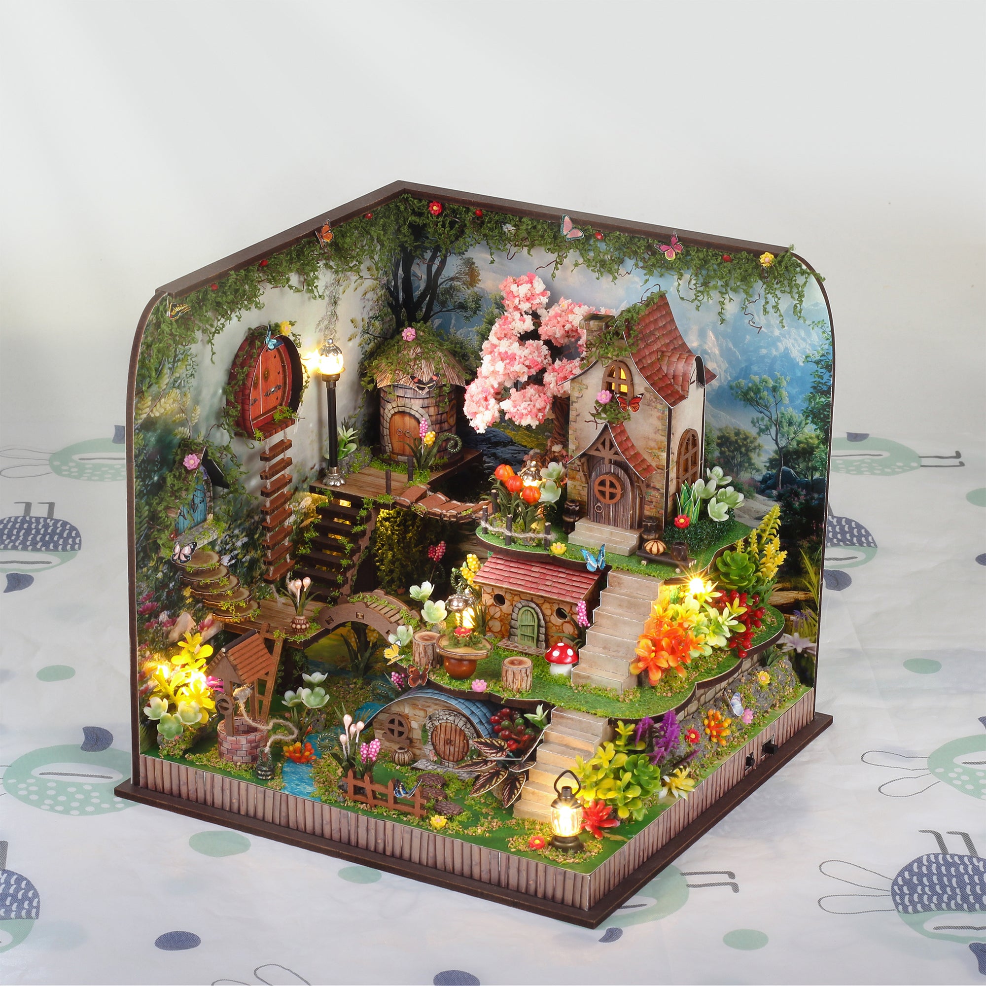 Miniature forest cabin diorama with pink blossoms, lantern lights, and tiny garden
