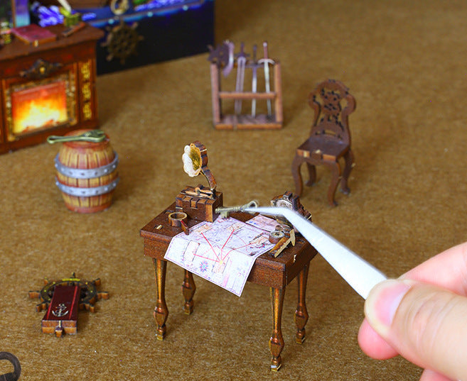 Miniature pirate accessories on tabletop; hand guides a small paper map at a wooden desk