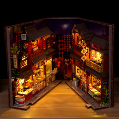 Miniature book nook kit with lit night market stalls, lanterns, and small storefronts inside wooden frame