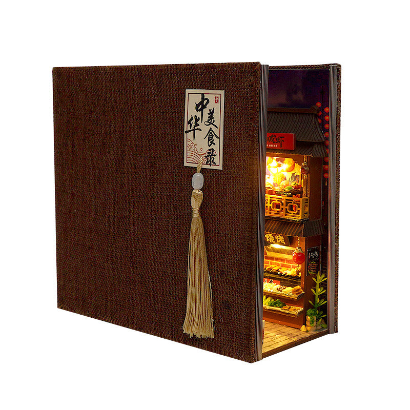 Miniature book nook kit closed, dark cover with hanging tassel and window showing warm-lit interior