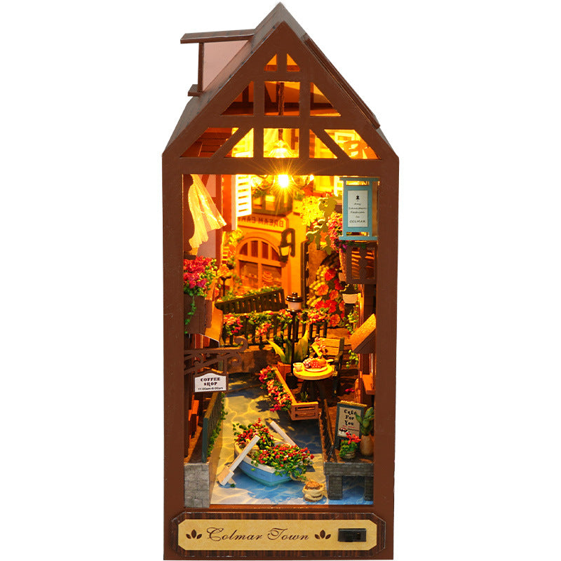Miniature book nook house display with warm light interior and floral walkway