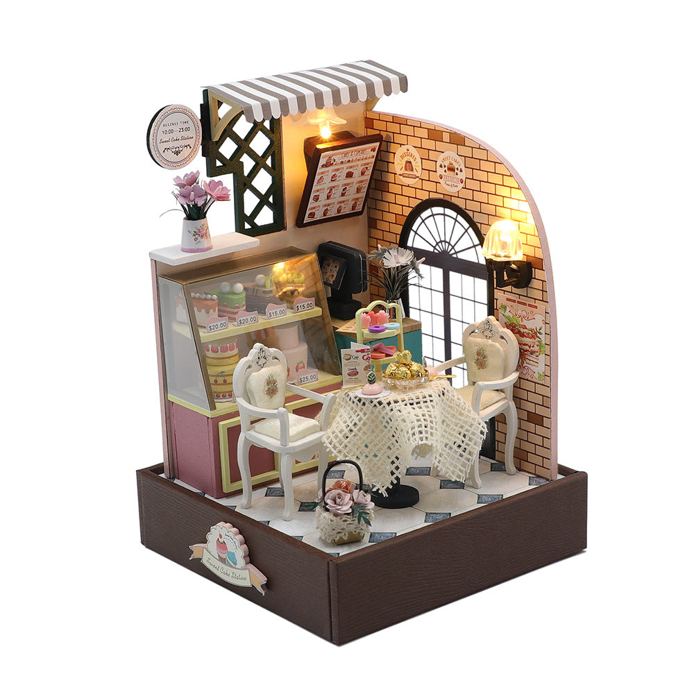 Light-up miniature bakery diorama with brick wall, shop window, striped awning and tiny chairs