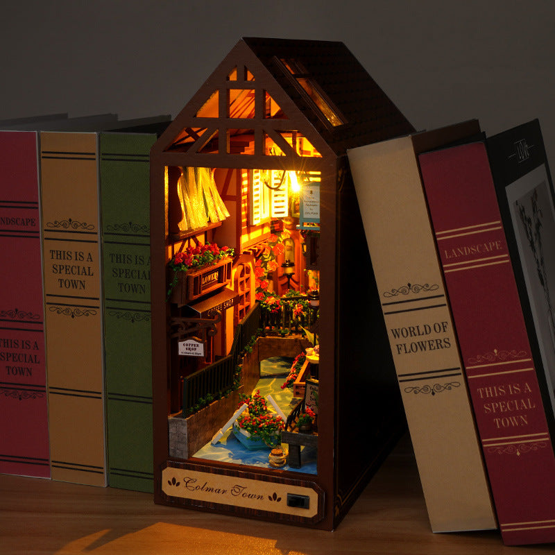 Miniature book nook house with warm interior lights and flower-lined walkway