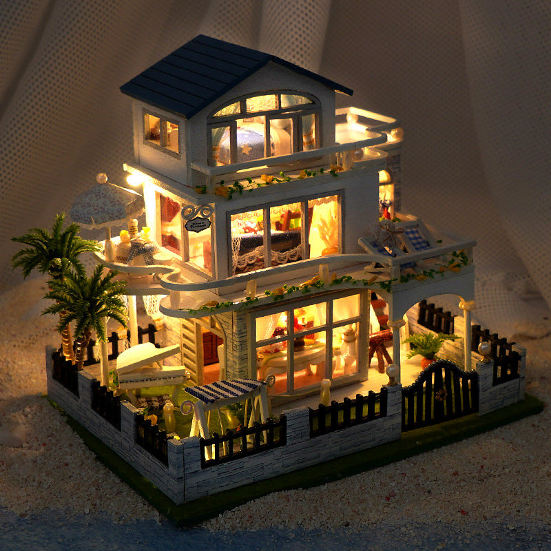 Lit miniature two-story dollhouse with blue roof, arched windows, and furnished rooms