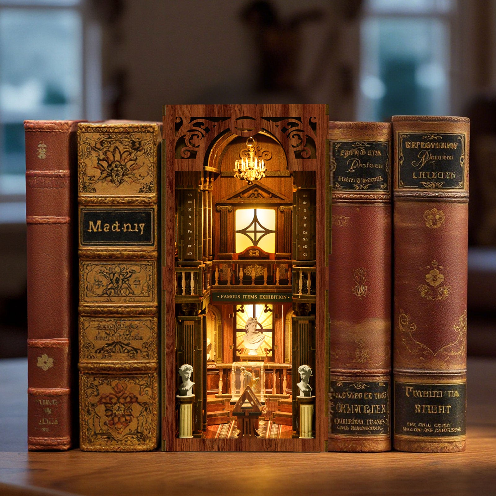 A miniature diorama of a library or bookcase, with a clock and other decorative elements, is displayed between two old books on a wooden surface.