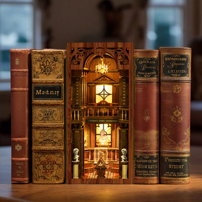 A miniature diorama of a library or bookcase, with a clock and other decorative elements, is displayed between two old books on a wooden surface.