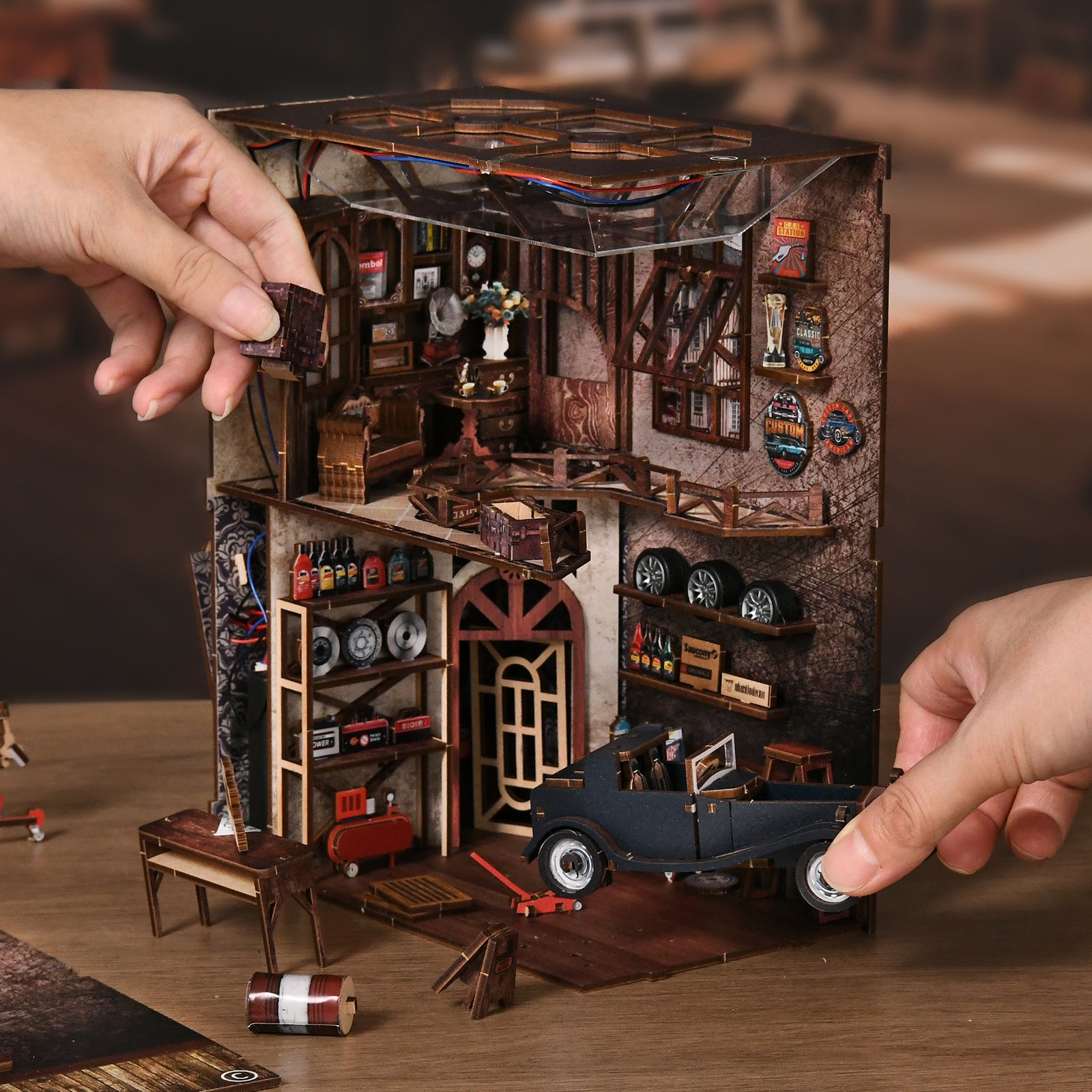 Miniature repair shop model with tools and carts, hands attaching parts