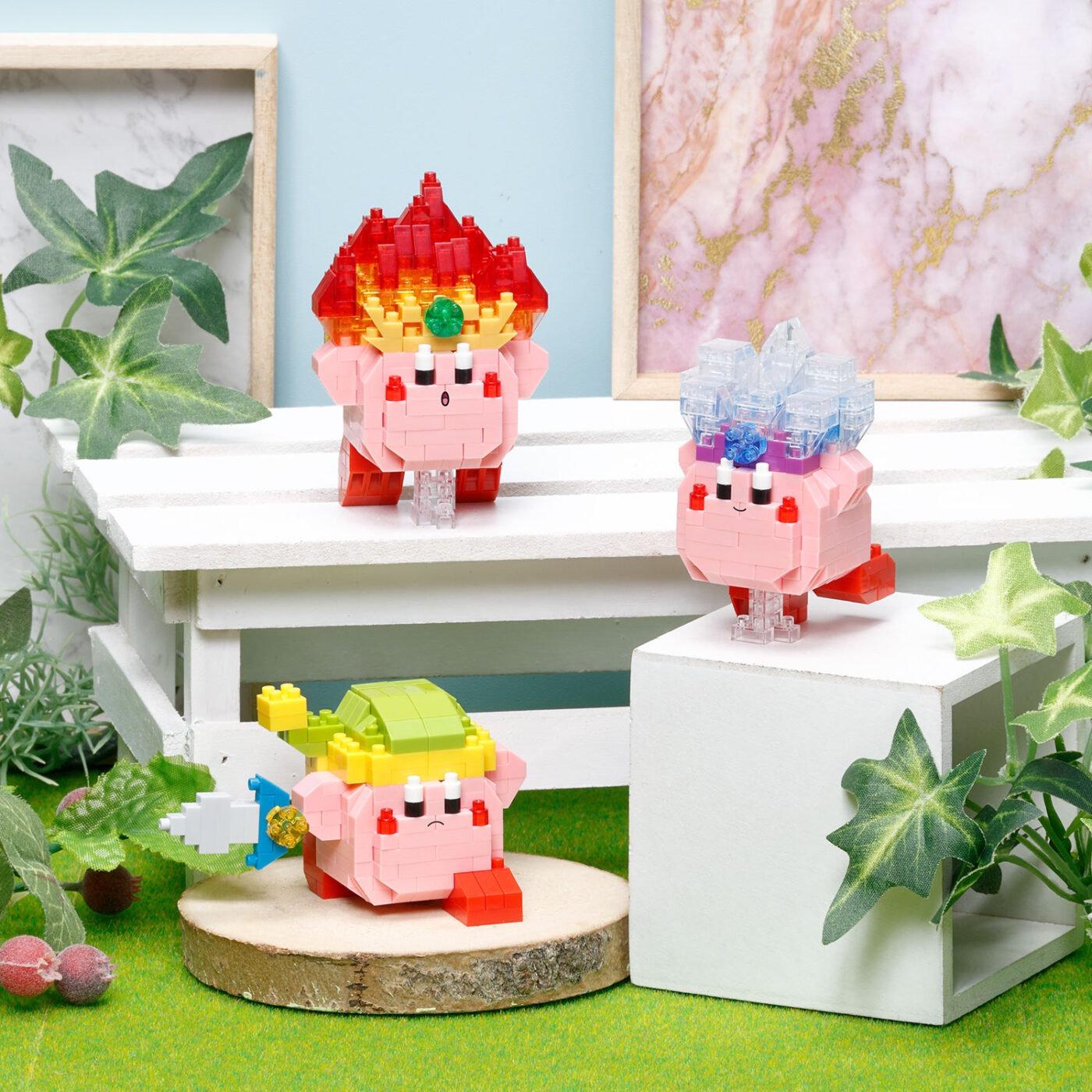 Three nano building block characters on a white shelf, pink, red, and clear blue