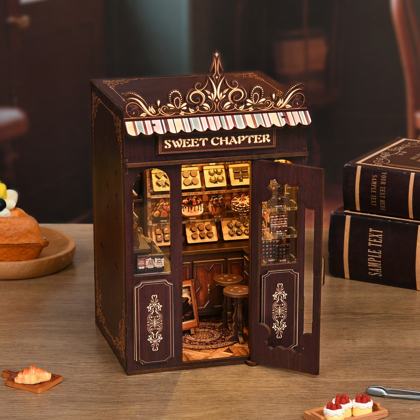 A miniature model of a small bakery shop, with a sign that reads "Sweet Chapter", displayed on a wooden table.